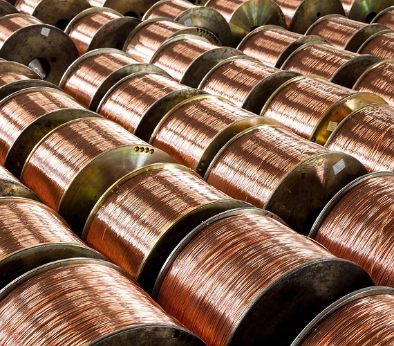 A tightly-packed grid of large spools wound with bright, bare copper wire in an industrial warehouse
