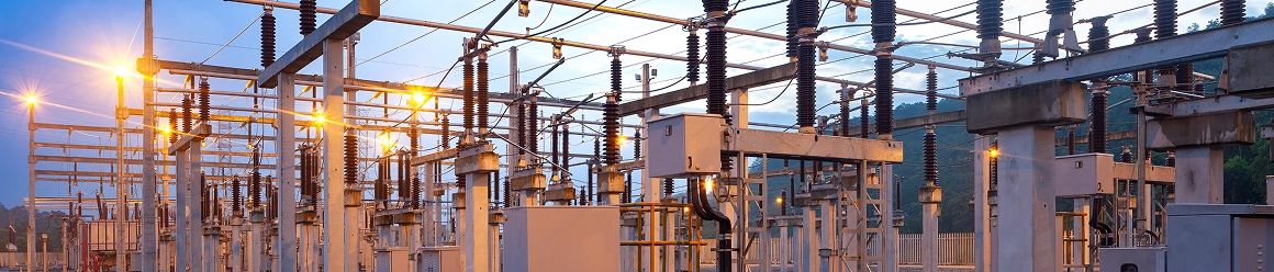 An electric power substation with insulators, transformers, and metal frameworks illuminated at twilight