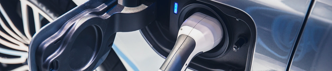 Close-up of a white charging plug connected to the charging port of an electric vehicle with a blue indicator light