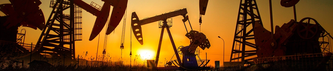 Silhouettes of multiple oil pump jacks against a bright orange and yellow sunset