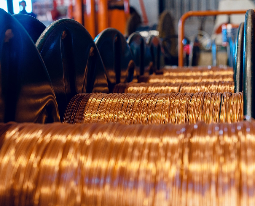 Extreme close up of numerous bright copper wires tightly wound around a large metallic spool in an industrial setting, with a subtle glow on the metal
