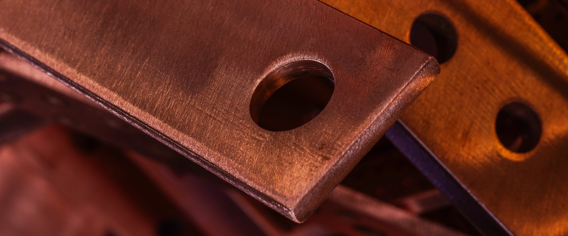 A close-up view of a thick, flat copper bar or electrical connector with a smooth, machined hole in the corner