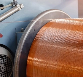 Close up of bare copper wire being spooled onto a large metal reel in an industrial drawing or winding machine.