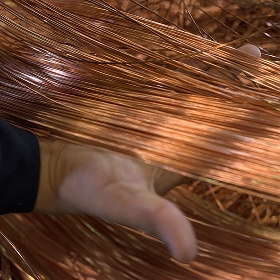 A person's hand holding and separating a large bundle of fine, bare copper wires in an industrial setting