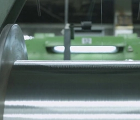 Close up of a thin metal conductor wire being spooled onto a large, smooth metallic reel in a manufacturing environment.