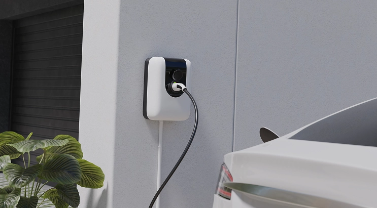 A modern electric vehicle charging unit installed on a home garage wall, with a white car visible nearby
