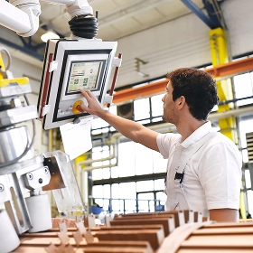 A factory technician in a white shirt operating a touchscreen control panel on a large piece of automated industrial machinery